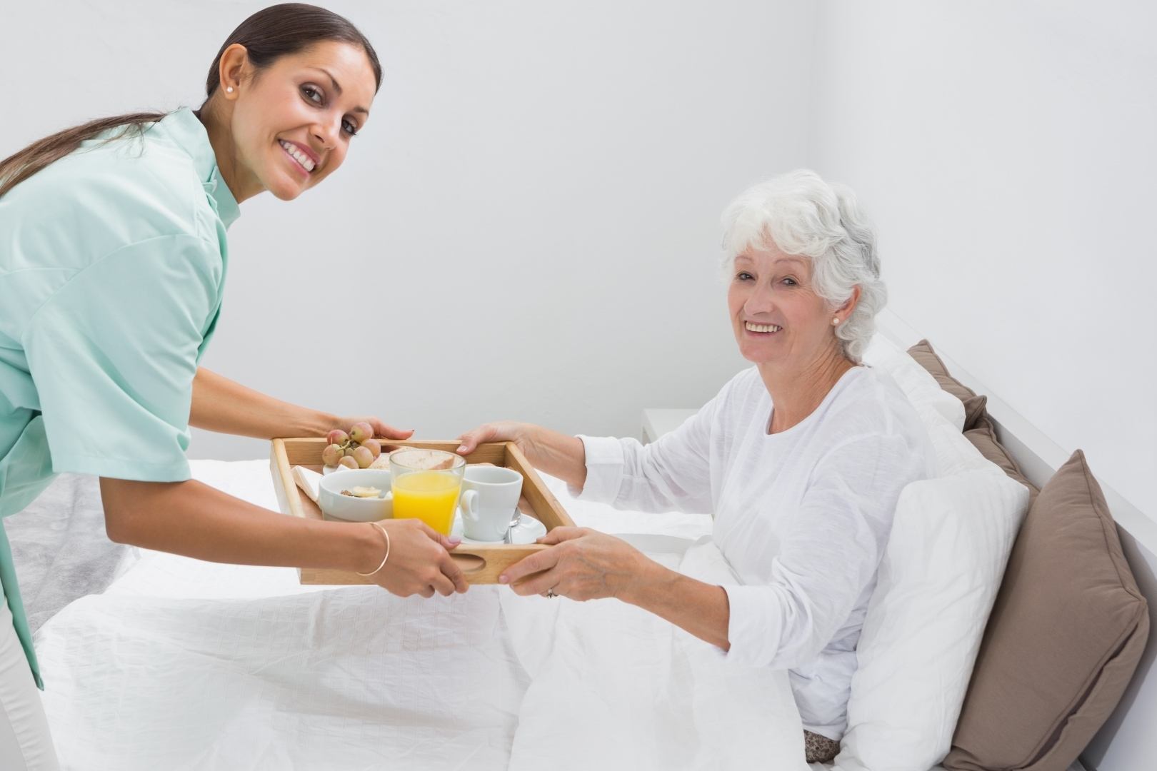 Home nurse giving a breakfast to the old woman on the bed