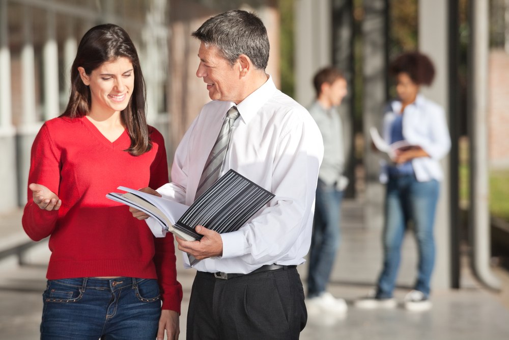 Mature male teacher and student discussing over book on college campus