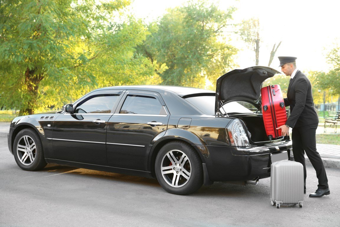 Chauffeur putting suitcase in car trunk